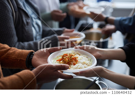 Close up of hands holding plastic plate with rice, unrecognizable volunteer helping refugees at soup kitchen Close up of hands holding plastic plate with rice, unrecognizable volunteer helping refugees at soup kitchen 110640432