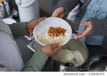 Top view closeup of woman giving hot meals to refugees at soup kitchen, focus on hands holding plate with rice 110640470