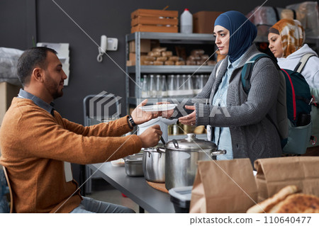 Side view portrait of Middle Eastern woman wearing hijab receiving hot meal at soup kitchen or refugee help center Side view portrait of Middle Eastern woman wearing hijab receiving hot meal at soup kitchen or refugee help center 110640477