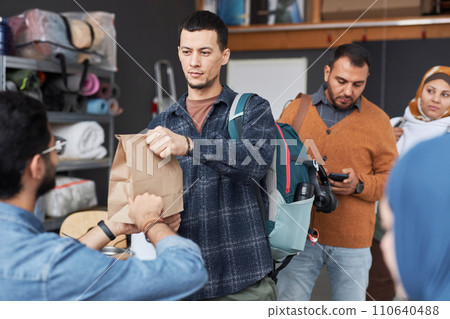 Waist up portrait of young man standing in line at refugee help center receiving food and donations 110640488