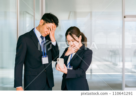A businessman and a businesswoman are shocked when they look at their smartphones (trouble, bad news, failure, rejection, rejection) 110641291