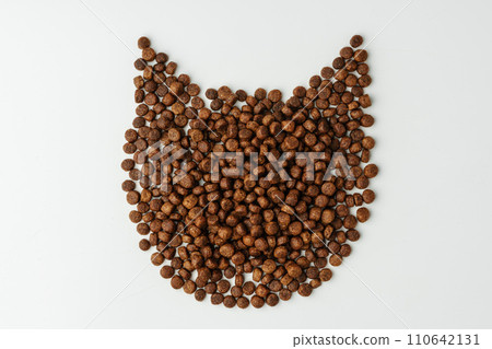 Dry cat food laid out in the shape of a cat's head on white background 110642131