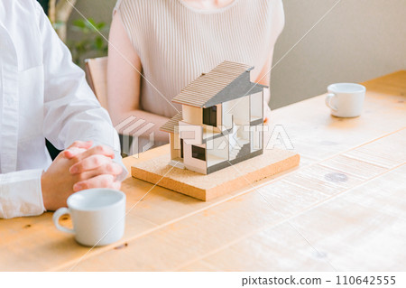 A young couple looking at a house model and considering the floor plan of their home (consultation meeting, house builder, detached house) A young couple looking at a house model and considering the floor plan of their home (consultation meeting, house builder, detached house) 110642555