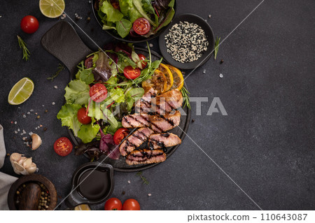 sliced grilled Organic Tuna Steak on black ceramic serving dish with salad on a table 110643087