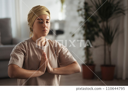 Young woman with cancer taking yoga and meditating in her apartment. Strong female patient calming her mind with easy exercise. Concept of mental health and cancer. 110644795