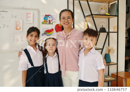 Portrait of happy teacher and her three pupils standing in class 110646757