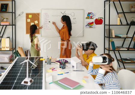 Kids in vr glasses watching educational video when classmate talking with teacher Kids in vr glasses watching educational video when classmate talking with teacher 110646837