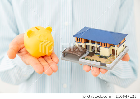 Hand of a middle-aged woman holding a house model and a pig piggy bank Hand of a middle-aged woman holding a house model and a pig piggy bank 110647125