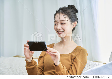 一位年輕女子穿著家居服,看著智慧型手機螢幕 一位年輕女子穿著家居服,看著智慧型手機螢幕 110647357
