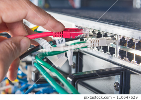 closeup of hand of administrator connecting network cable into switch 110647629