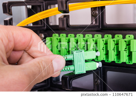 Hand of computer technician connecting fiber optics cable into data switch Hand of computer technician connecting fiber optics cable into data switch 110647671