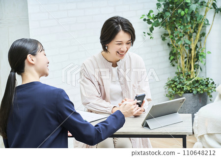 A woman in a suit explaining to a woman in plain clothes 110648212