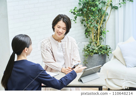 A woman in a suit explaining to a woman in plain clothes 110648214