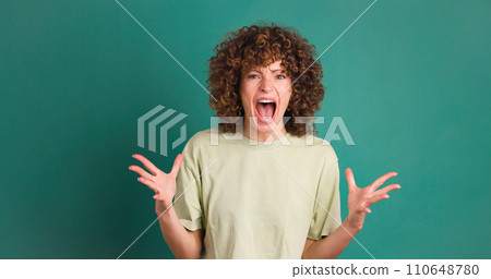 Shocked young woman showing stretched hands with palms on green background Shocked young woman showing stretched hands with palms on green background 110648780