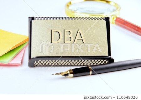 DBA text on a gold plastic card with convex text next to office supplies on a white background DBA text on a gold plastic card with convex text next to office supplies on a white background 110649026