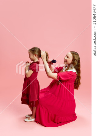 Girly moments. Beautiful young mother brushing daughter's hair, doing hairstyle against pink studio background. Mother's Day, International Happiness Day 110649477