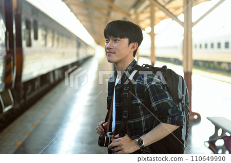 Portrait of happy man tourist with backpack waiting train at railroad station platform Portrait of happy man tourist with backpack waiting train at railroad station platform 110649990