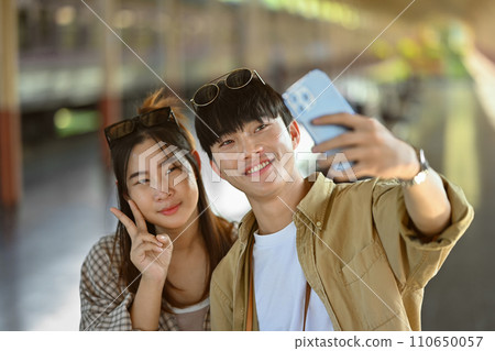 Attractive young couple taking a selfie with mobile phone at train station. Travel and lifestyle concept Attractive young couple taking a selfie with mobile phone at train station. Travel and lifestyle concept 110650057