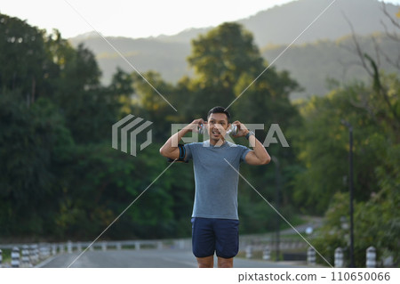 Active sporty man listening to music through headphones while running in the morning 110650066