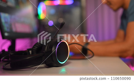 Close up of headset on desk with male gamer sitting in background. Gamer and technology concept Close up of headset on desk with male gamer sitting in background. Gamer and technology concept 110650090