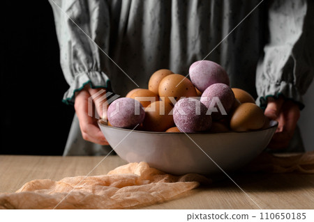 A girl in a vintage dress holds a large bowl of dyed eggs 110650185