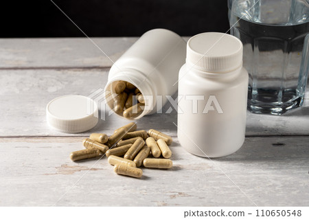 Transparent pills in white plastic bottle and glass of water. Capsules, collagen, vitamins, pain killers or drugs 110650548