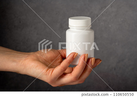 Female hand holding a white plastic bottle with pills. Capsules, collagen, vitamins, pain killers or drugs Female hand holding a white plastic bottle with pills. Capsules, collagen, vitamins, pain killers or drugs 110650550