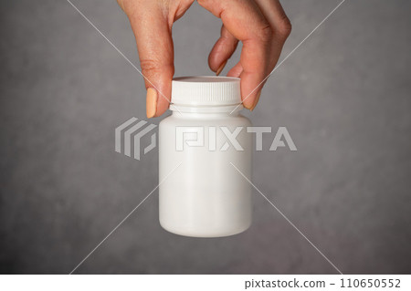 Female hand holding a white plastic bottle with pills. Capsules, collagen, vitamins, pain killers or drugs 110650552