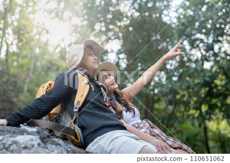 Cheerful romantic lesbian couple traveler with backpacks and siting relaxing while hiking in the mountains in summer Cheerful romantic lesbian couple traveler with backpacks and siting relaxing while hiking in the mountains in summer 110651062