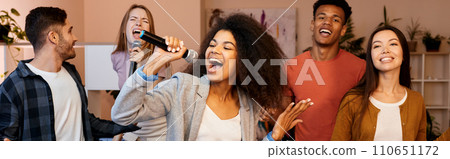 Singing means happiness. Pretty mixed race girl looking enthusiastic while holding microphone and singing at karaoke party with best friends. Happy multicultural people spending time together 110651172