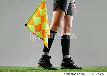 Cropped image of female legs, referee on field standing with flag to signal game rules against grey studio background Cropped image of female legs, referee on field standing with flag to signal game rules against grey studio background 110652307