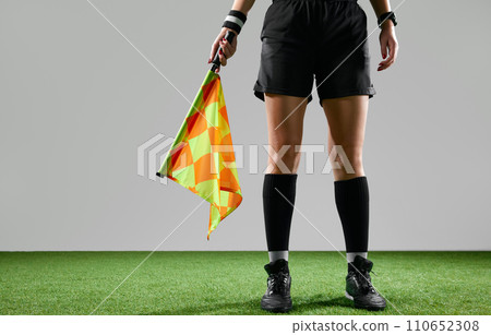 Cropped image of female legs, referee on field standing with flag to signal game rules against grey studio background Cropped image of female legs, referee on field standing with flag to signal game rules against grey studio background 110652308