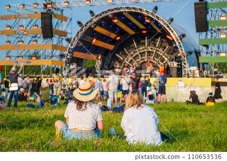 Summer festival atmosphere with audience enjoying live music concert outdoors, sitting on grass Summer festival atmosphere with audience enjoying live music concert outdoors, sitting on grass 110653536