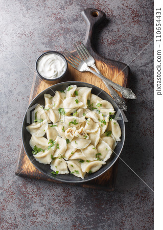 Boiled dumplings small pierogi or uszka filled with wild forest mushrooms and cabbage closeup on the plate. Vertical top view 110654431