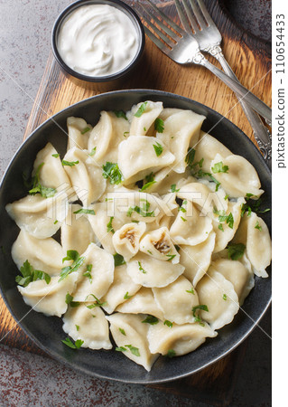 Traditional Polish ravioli dumplings or uszka served with sour cream closeup on the plate on the table. Vertical top view 110654433