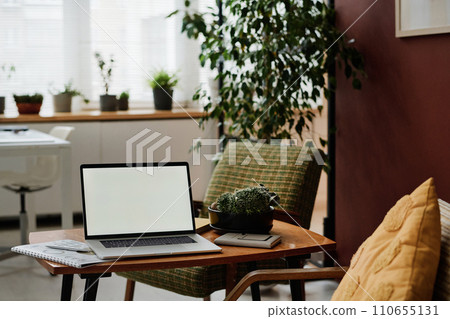 Laptop with white screen mockup placed on table in modern office with greenery and vintage furniture 110655131