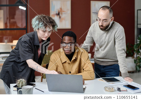 Young female office worker and her biracial male colleagues examining information on laptop screen 110655141