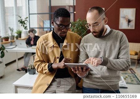 Biracial male workers looking at digital tablet screen and discussing business project 110655169