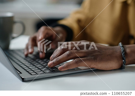 Closeup of hands of african american man typing on laptop keyboard while sitting at desk Closeup of hands of african american man typing on laptop keyboard while sitting at desk 110655207