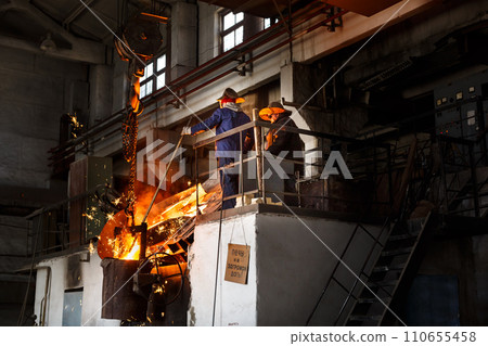 Industrial workers in protective gear operate furnace, handling molten metal at steel mill. Teamwork in heavy industry, hot steel pouring in foundry. Laborers ensure manufacturing process safety. Industrial workers in protective gear operate furnace, handling molten metal at steel mill. Teamwork in heavy industry, hot steel pouring in foundry. Laborers ensure manufacturing process safety. 110655458