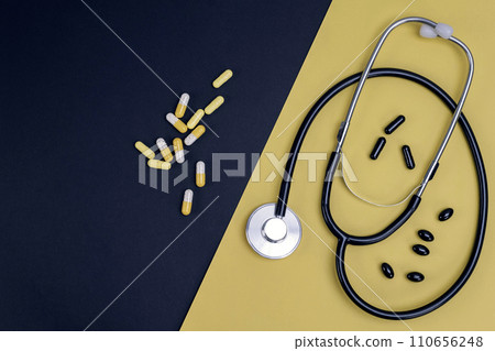 Stethoscope and capsules on yellow and black background 110656248