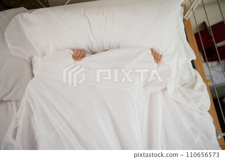 Scared little child hiding under white duvet while waking up from bad dream, sleeping, feeling fear, afraid of nightmare 110656573