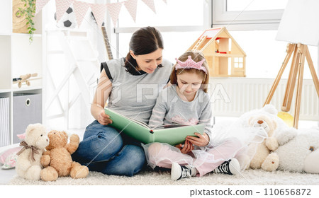Lovely woman showing photo album to little girl in beautiful children's room Lovely woman showing photo album to little girl in beautiful children's room 110656872