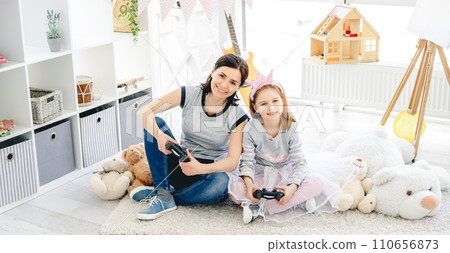Cute little girl playing video game with mother in playroom 110656873