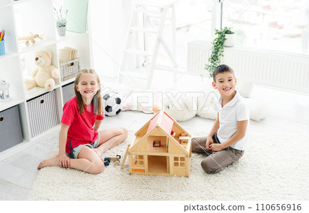 Happy kids having fun with wooden dollhouse in play room, top view Happy kids having fun with wooden dollhouse in play room, top view 110656916