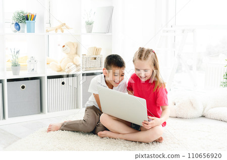 kids playing laptop sitting on floor in light room 110656920