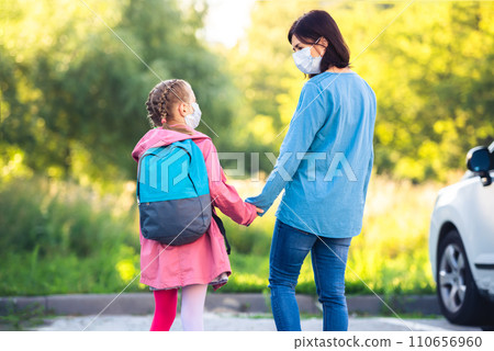 Mother meeting primary schoolgirl after classes on car parking outdoors during virus epidemic 110656960