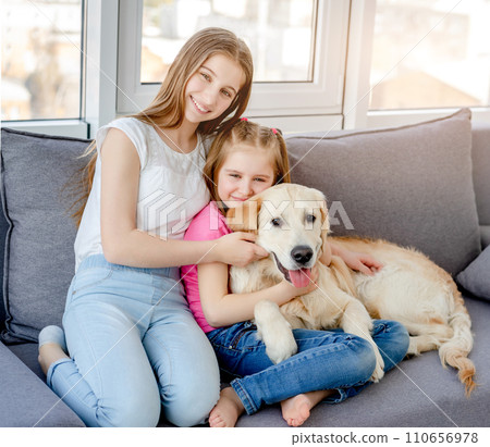 Smiling girls cuddling lovely dog in light room Smiling girls cuddling lovely dog in light room 110656978