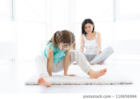 Attractive little girl trying to do yoga under supervision Attractive little girl trying to do yoga under supervision 110656994