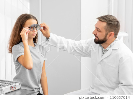 Doctor ophthalmologist holding equipment examinating teenager girl's eyes in the clinic Doctor ophthalmologist holding equipment examinating teenager girl's eyes in the clinic 110657014